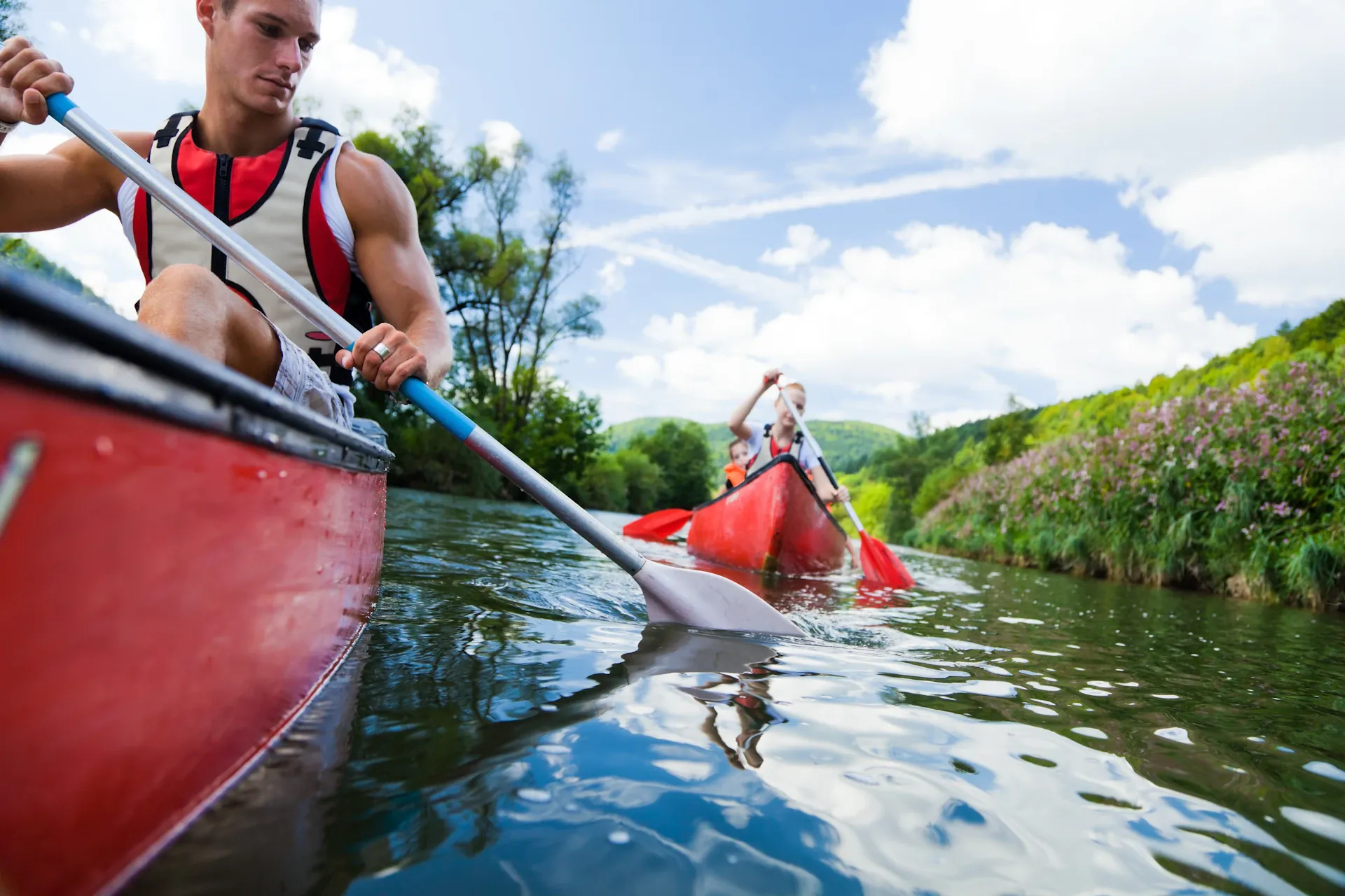 Friends canoeing together on a calm green river surrounded by lush trees on a sunny summer day